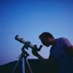 Man using telescope outside at night