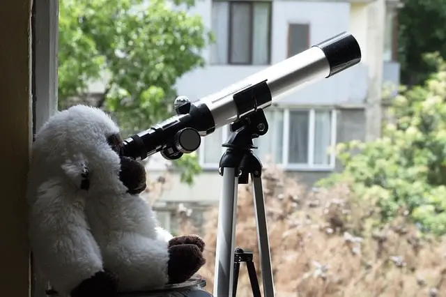 Telescope set up in window with a stuffed monkey